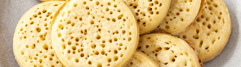 A close-up photograph of a plate of crumpets, which are a hole-covered spongey toasted bread treat commonly found in the United Kingdom.