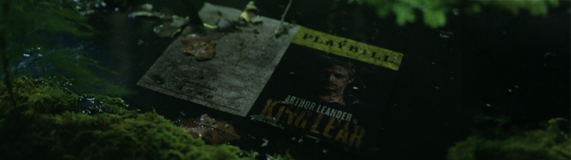 A playbill for King Lear with fictional actor Arthur Leander sits in a moss-covered puddle.
