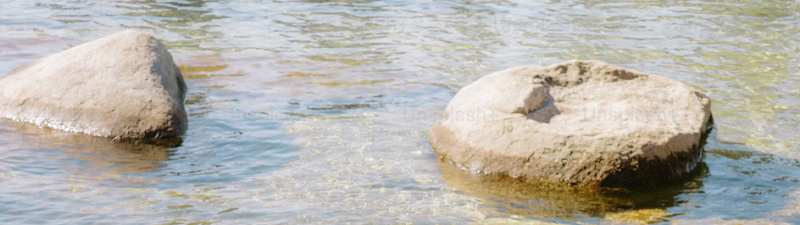 A photograph of two big rocks submerged in sand, with water around them.