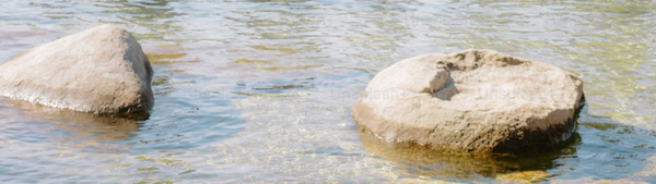 A photograph of two big rocks submerged in sand, with water around them.